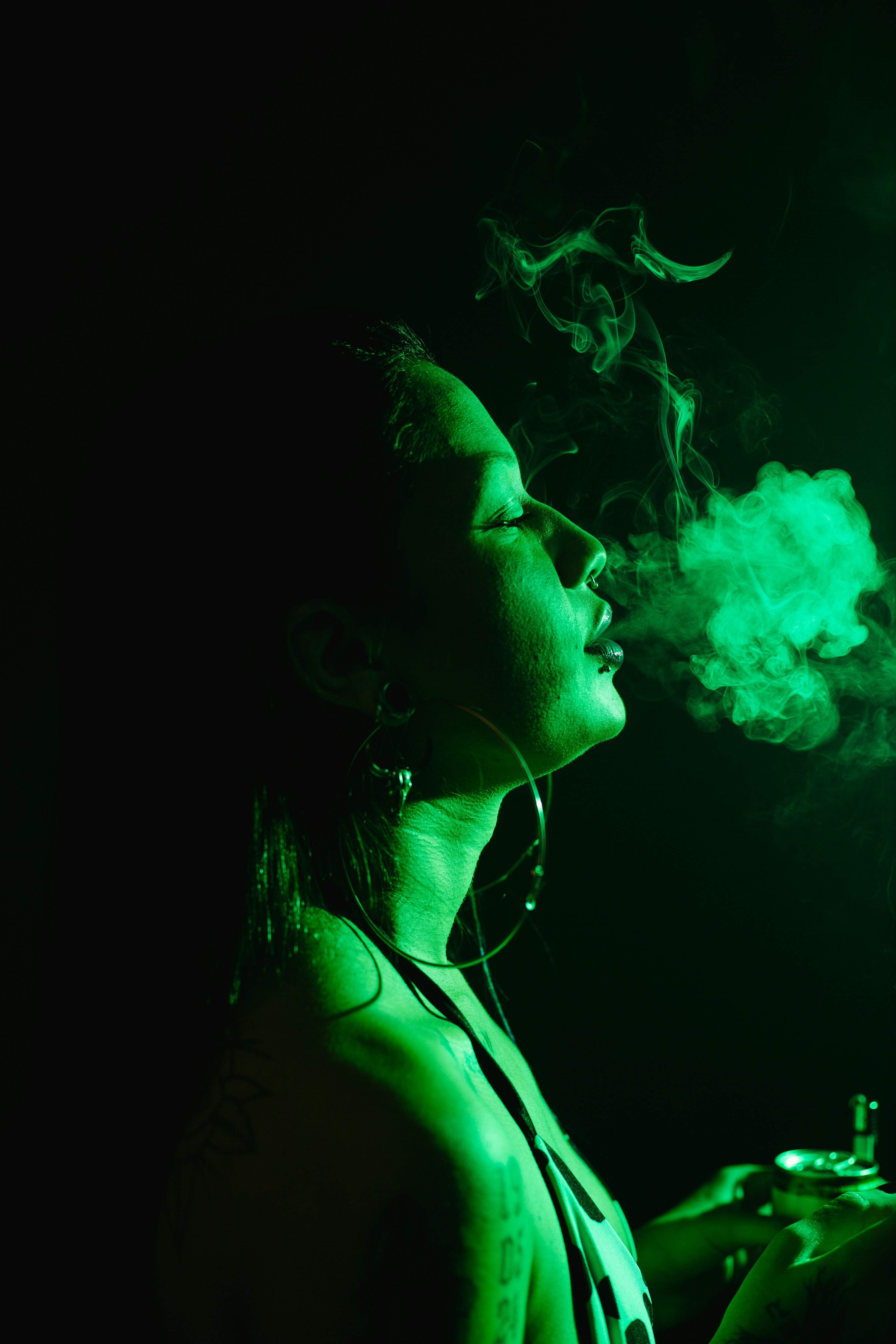 A woman is smoking a marijuana joint, exhaling smoke from her mouth.